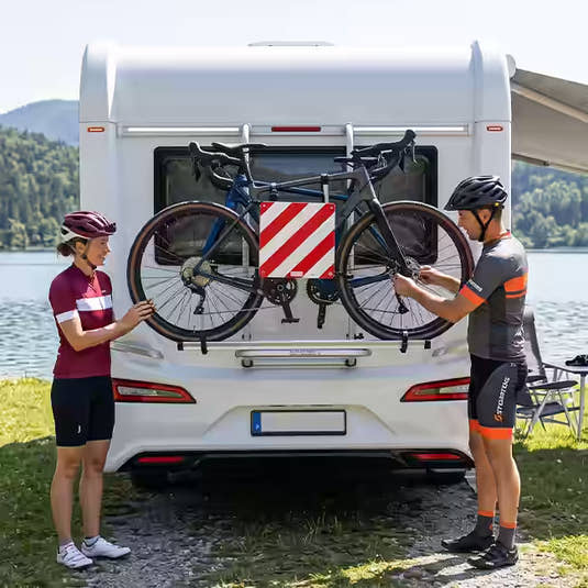 Two cyclists mounting bicycles onto a caravan-mounted bike rack