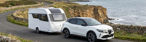 A white Alfa Romeo SUV towing a caravan along a UK coastal road