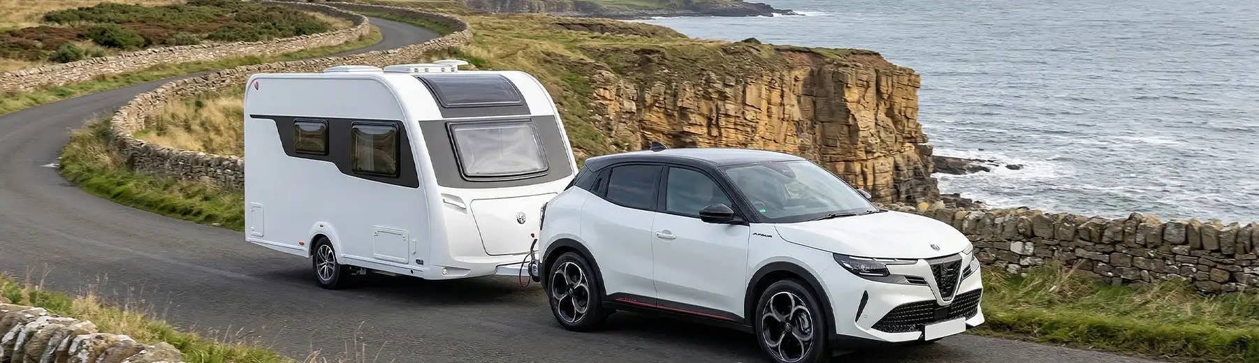 A white Alfa Romeo SUV towing a caravan along a UK coastal road