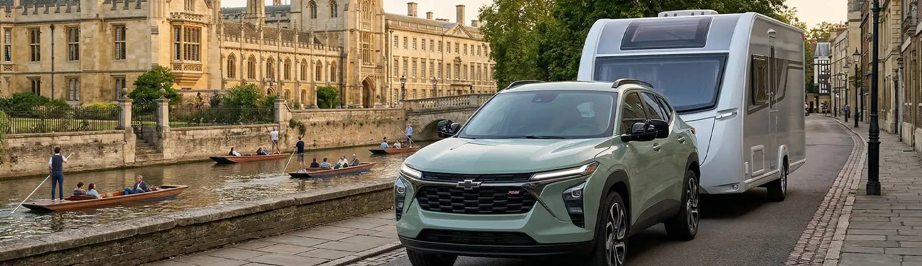 Green Chevrolet SUV towing a white caravan along a river with historic buildings in the background