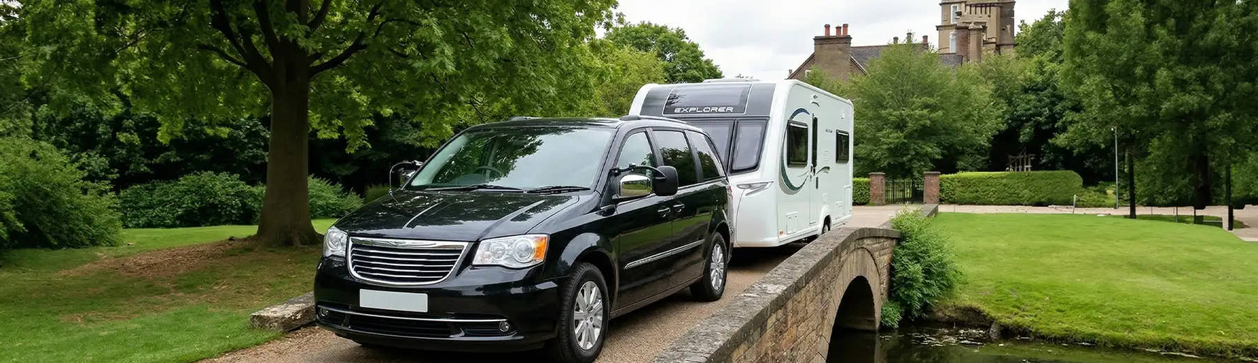 Black Chrysler Voyager MPV towing a white caravan on a bridge in a park-like setting
