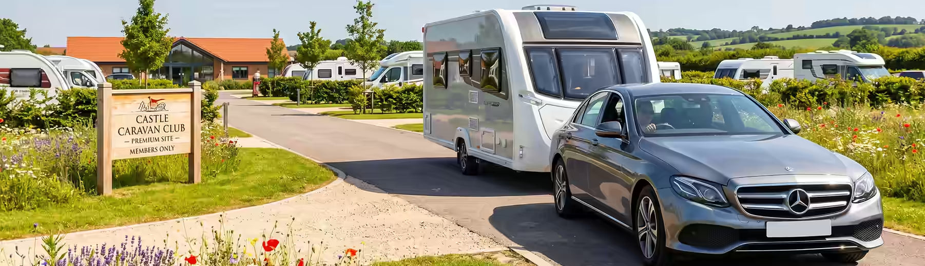 Caravan park with a silver car towing a caravan on a sunny day.