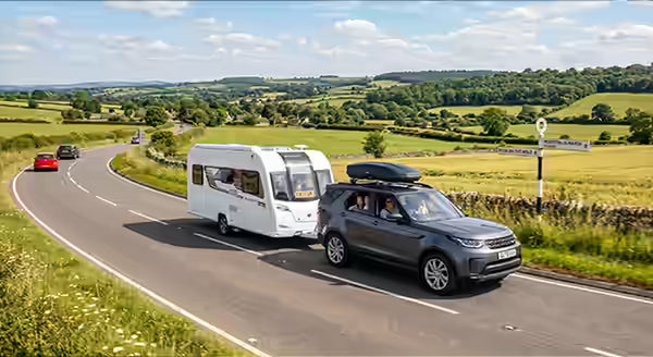 A modern SUV towing a caravan on a main A-road in the British countryside