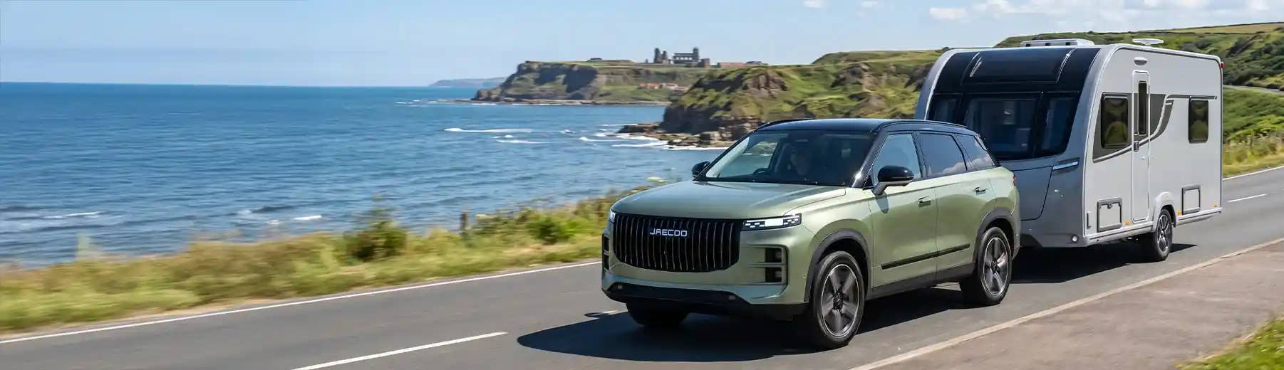 Green SUV towing a caravan along a UK coastal road 